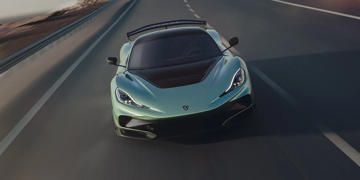 Aerial shot of the Rimac Nevera R at high speed on the highway, showcasing its two-tone carbon and mint-green finish with sharp aerodynamic lines.